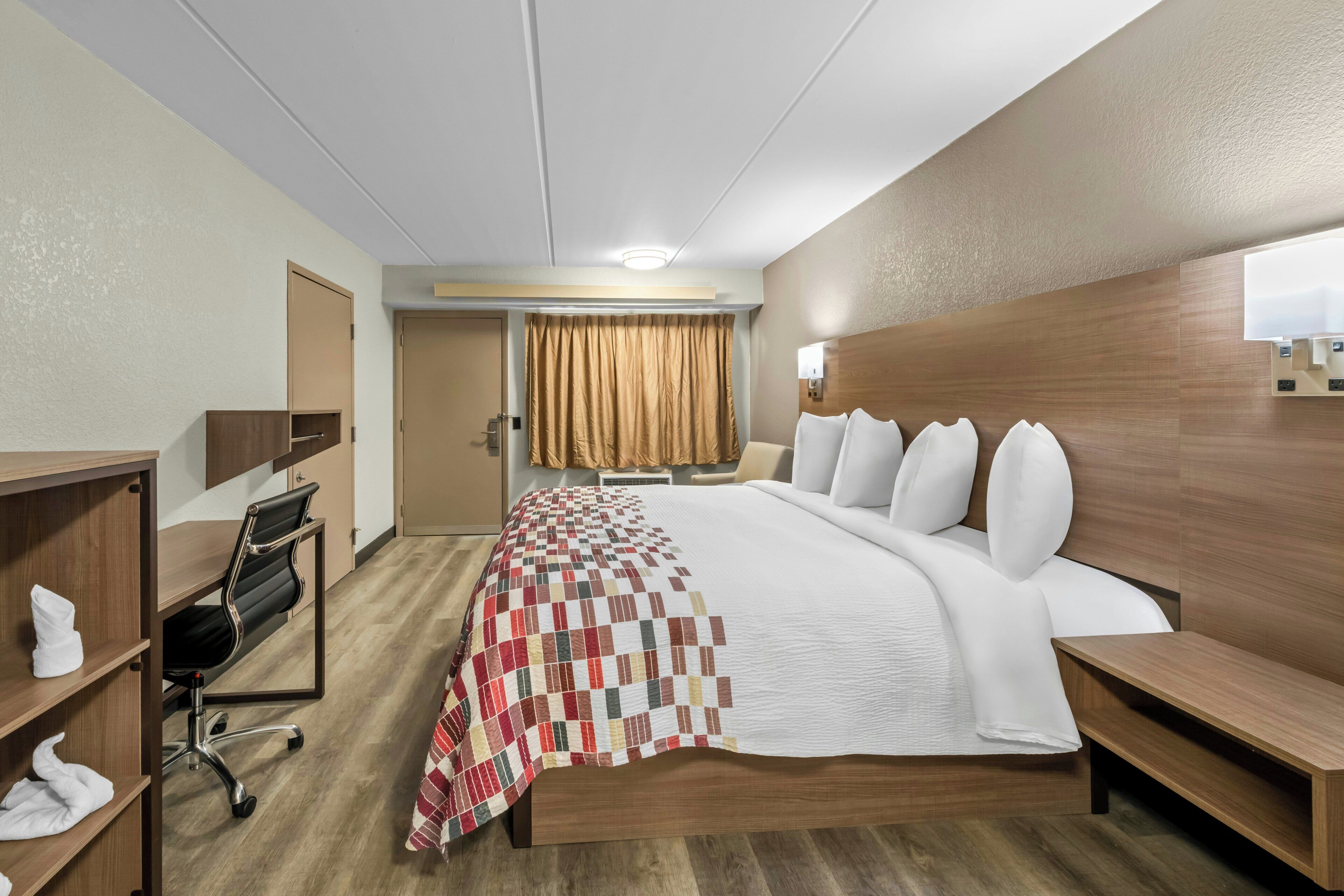 Une chambre d’hôtel avec un grand lit, un bureau avec une chaise, une armoire et une fenêtre avec des rideaux.