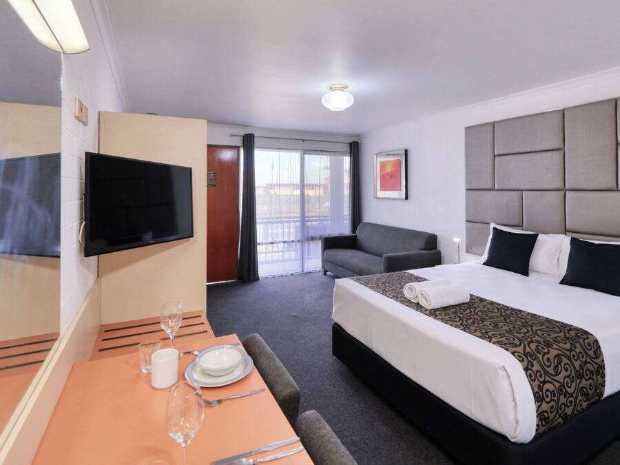A hotel room with a bed, a television, a dining area with a table set for two, and a balcony with a view.