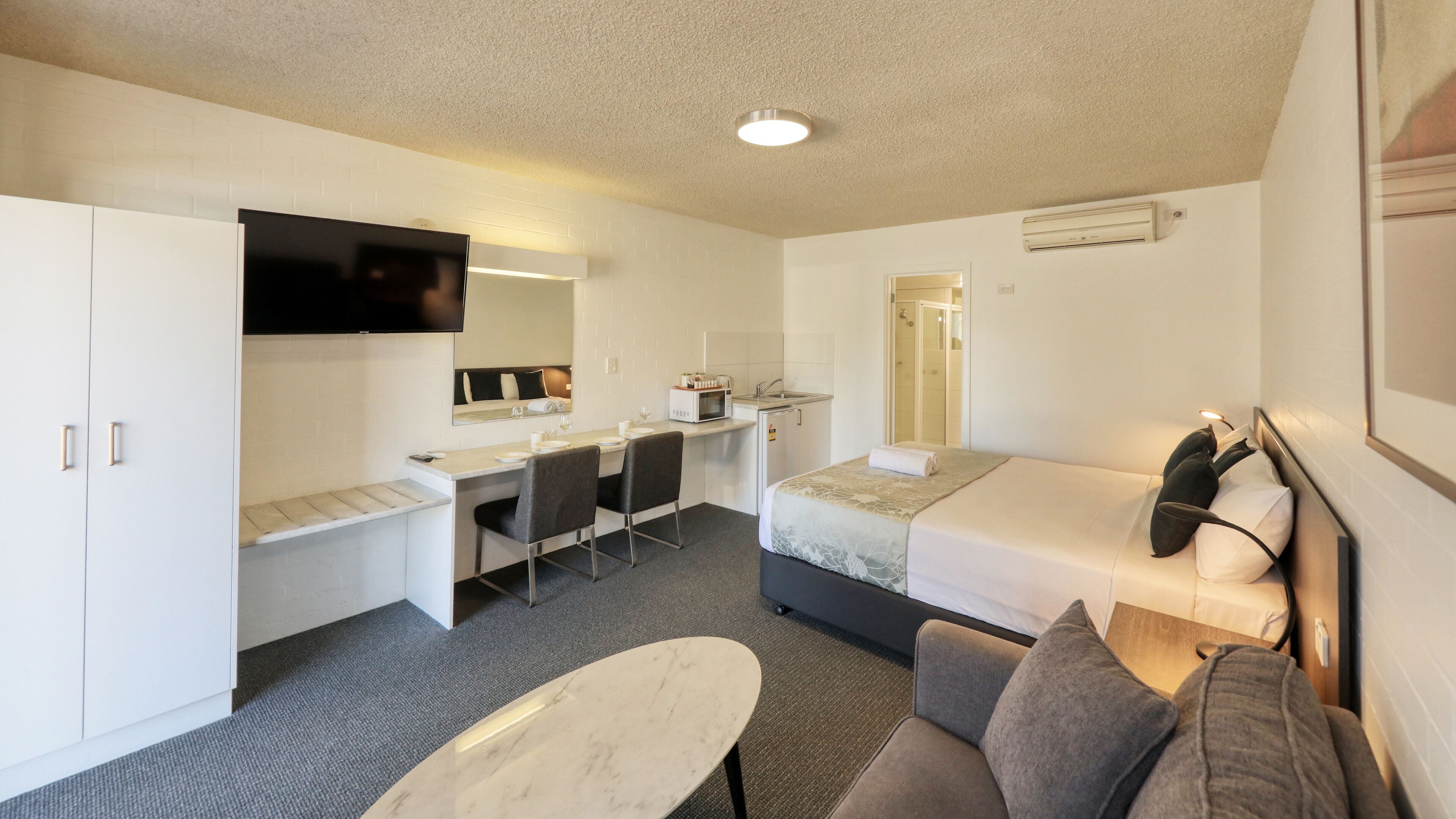 A compact hotel room with a kitchenette, a bed, a desk, and a TV.