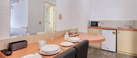 A compact kitchen with white brick walls, a microwave, a refrigerator, and a dining area with a table set for two.