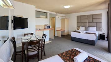 A hotel room with a bed, a desk with a microwave, a dining table with chairs, and a TV.
