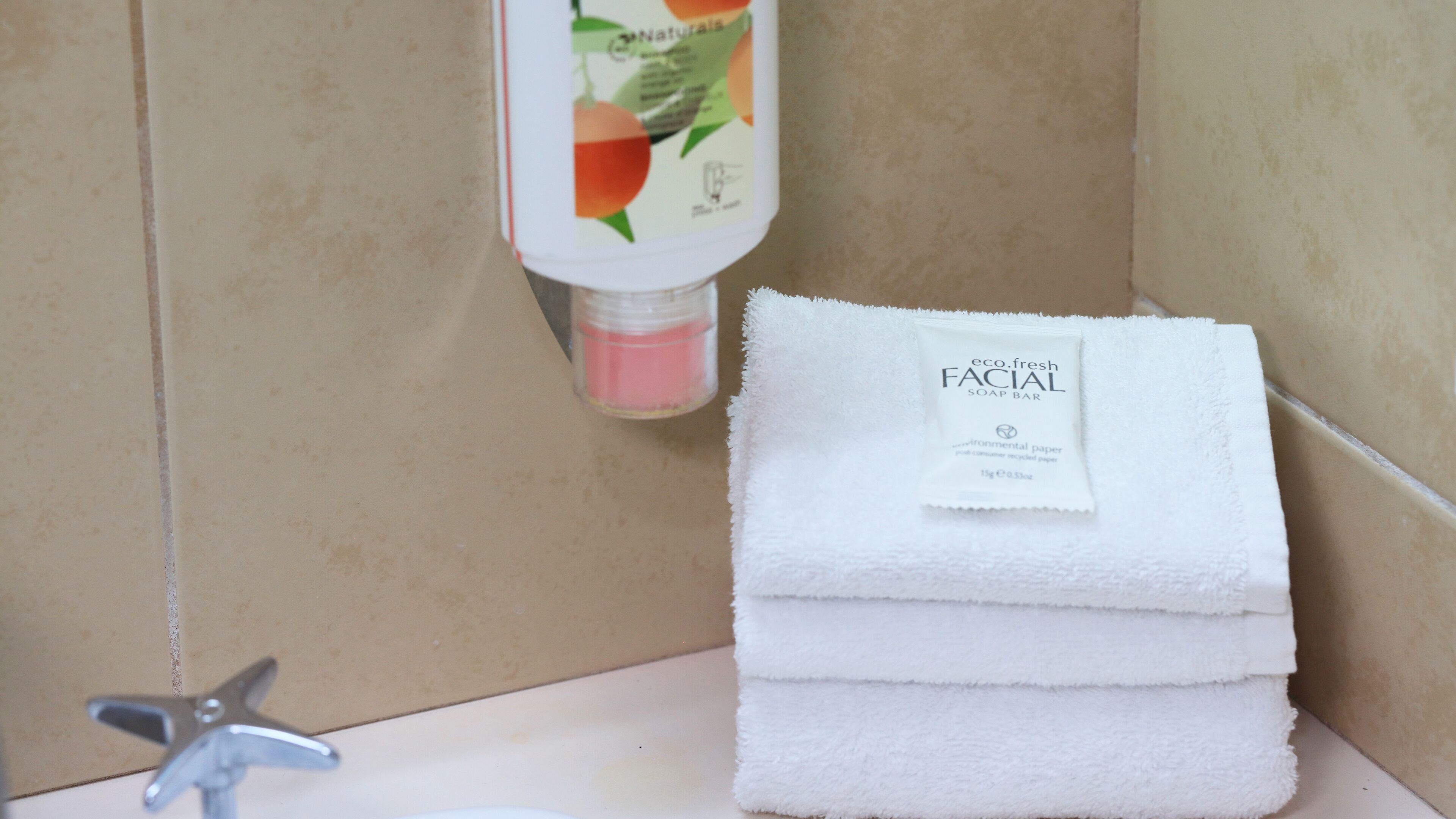 A bathroom with a sink, a towel dispenser, and a bottle of soap.
