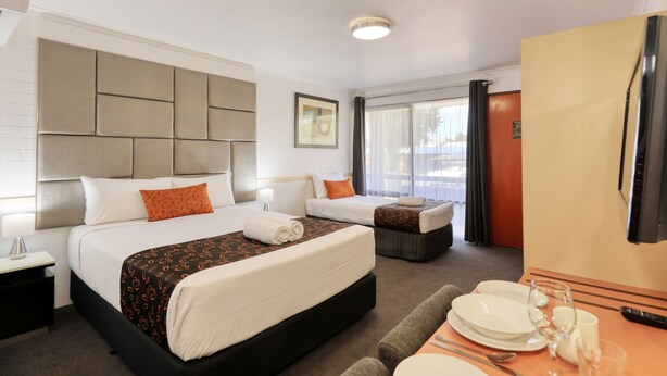 Quarto de hotel com duas camas, área de jantar com mesa posta para dois e uma janela grande com cortinas.