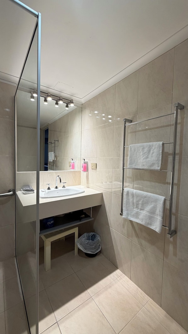 A modern bathroom with a glass shower enclosure, a vanity with a sink, and a towel rack.
