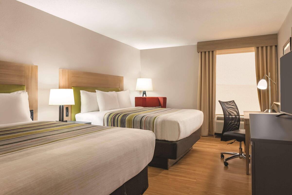 A hotel room with two beds, a desk, a chair, and a window with curtains.