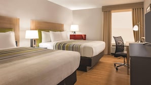 A hotel room with two beds, a desk, a chair, and a window with curtains.