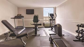 Une salle de sport équipée d’un tapis de course, d’un banc de développé couché, d’haltères et d’un vélo d’appartement.