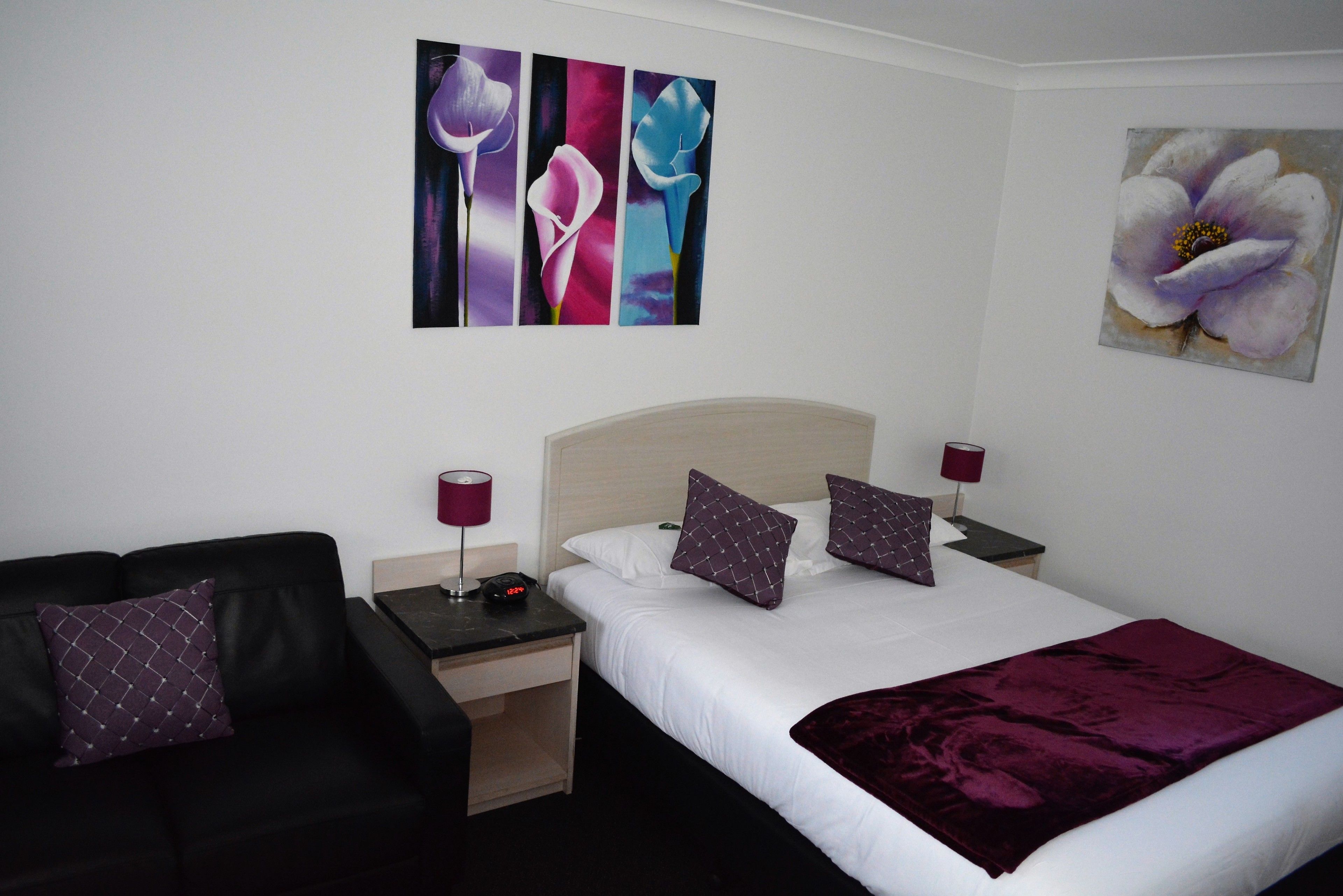 A hotel room with a bed, two nightstands, a black sofa, and artwork on the walls.