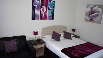 A hotel room with a bed, two nightstands, a black sofa, and artwork on the walls.