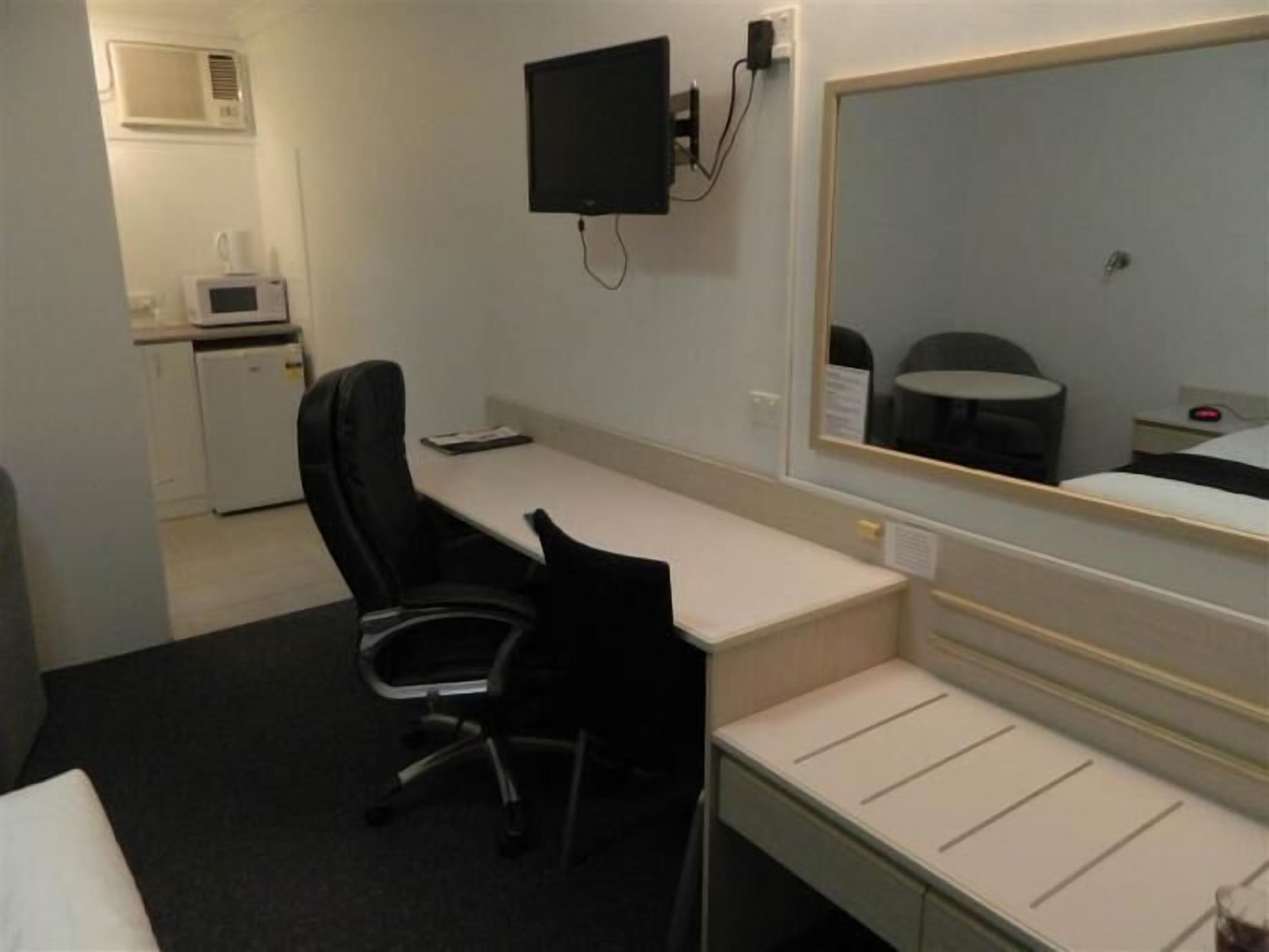 A hotel room with a desk, chair, bed, and a large mirror.