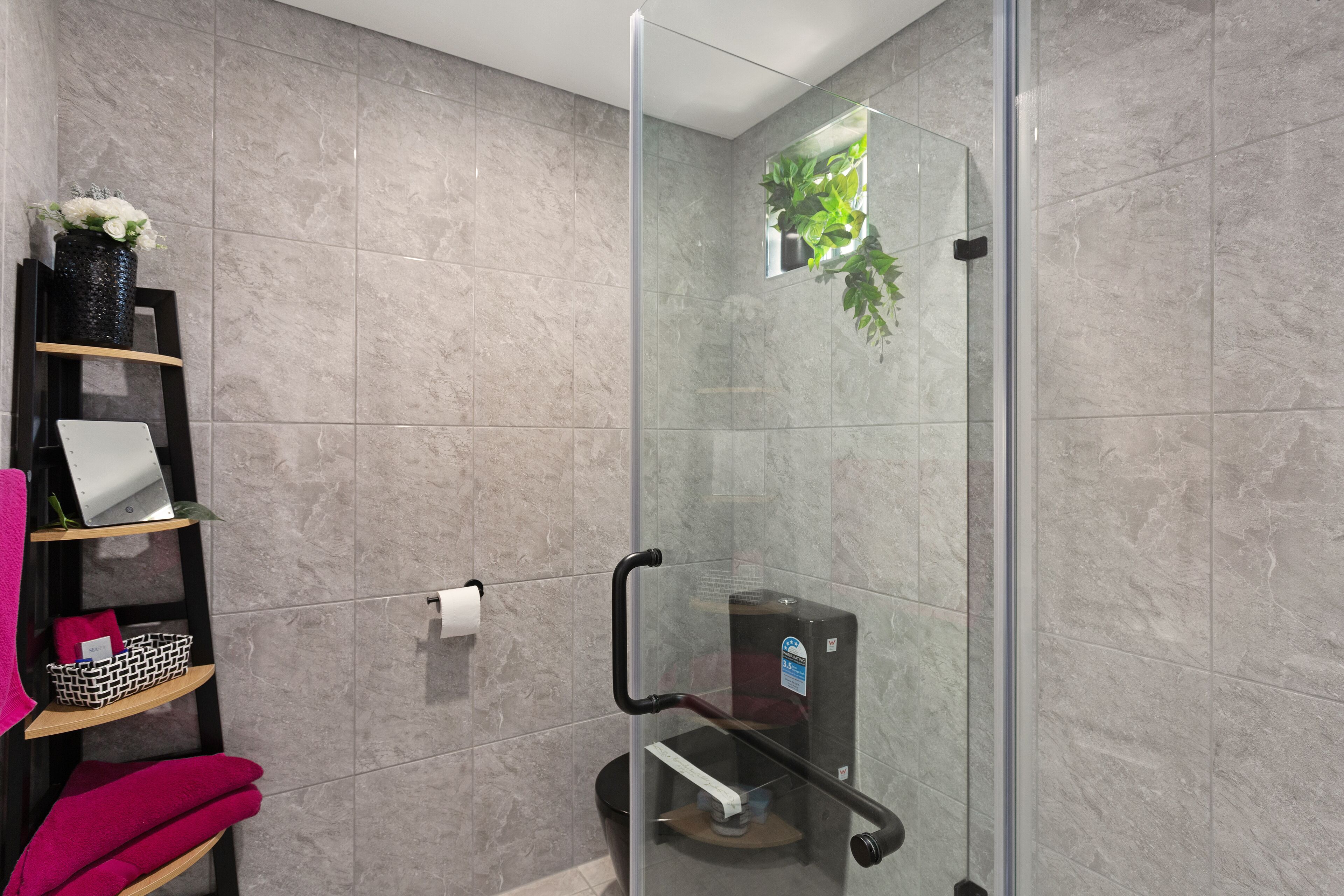 A modern bathroom with a glass shower enclosure, a shelf with towels, and a small potted plant.
