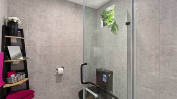 Un baño moderno con cabina de ducha de vidrio, repisa con toallas y una pequeña planta en maceta.