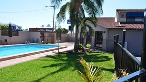 A swimming pool with a surrounding grassy area and a palm tree. - Alabaster Motor Inn Taree (Taree)