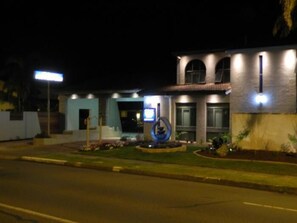 A modern building with a well-lit entrance, a landscaped garden, and a distinctive blue sculpture.