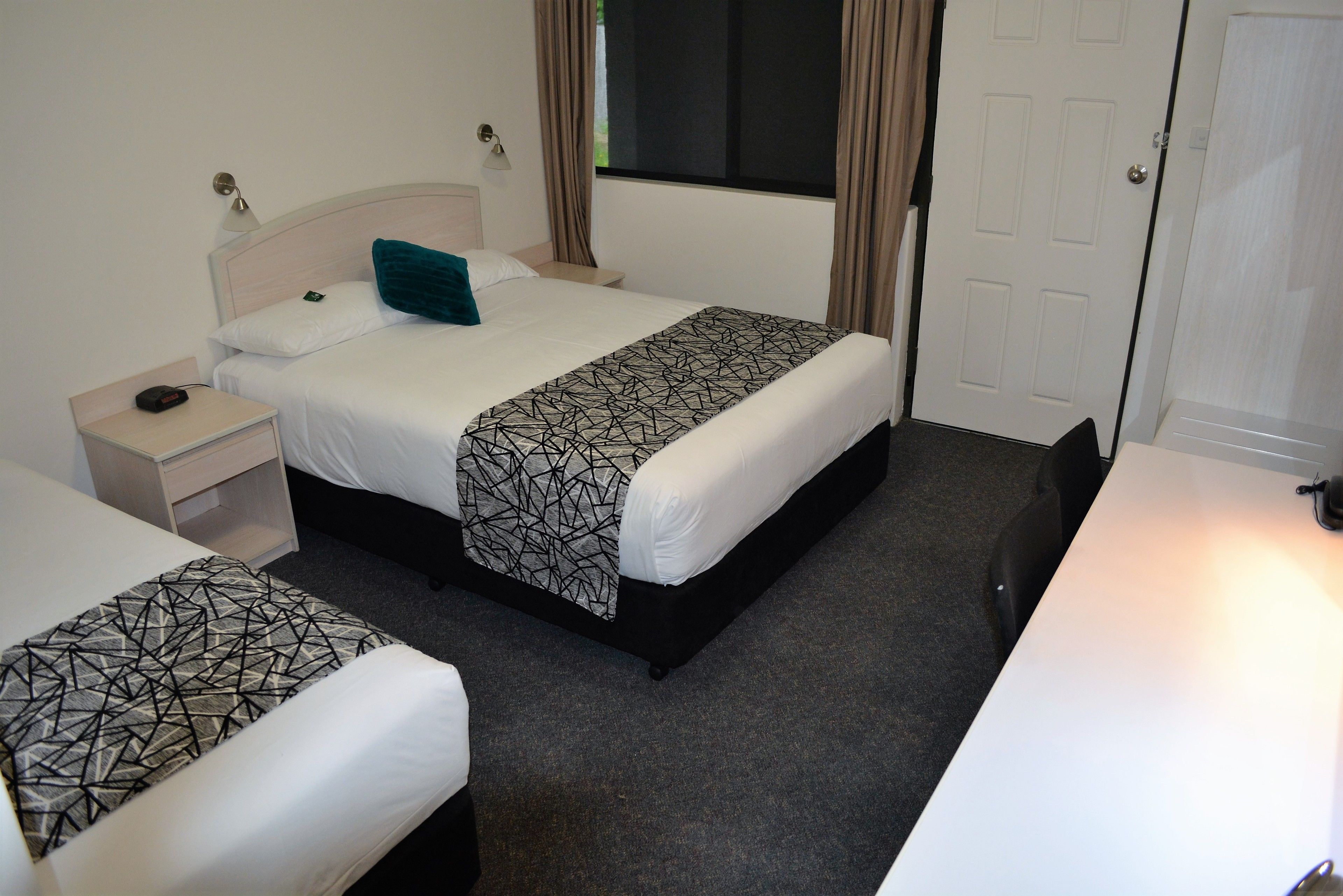 A hotel room with two beds, a nightstand, a desk, and a window with curtains.
