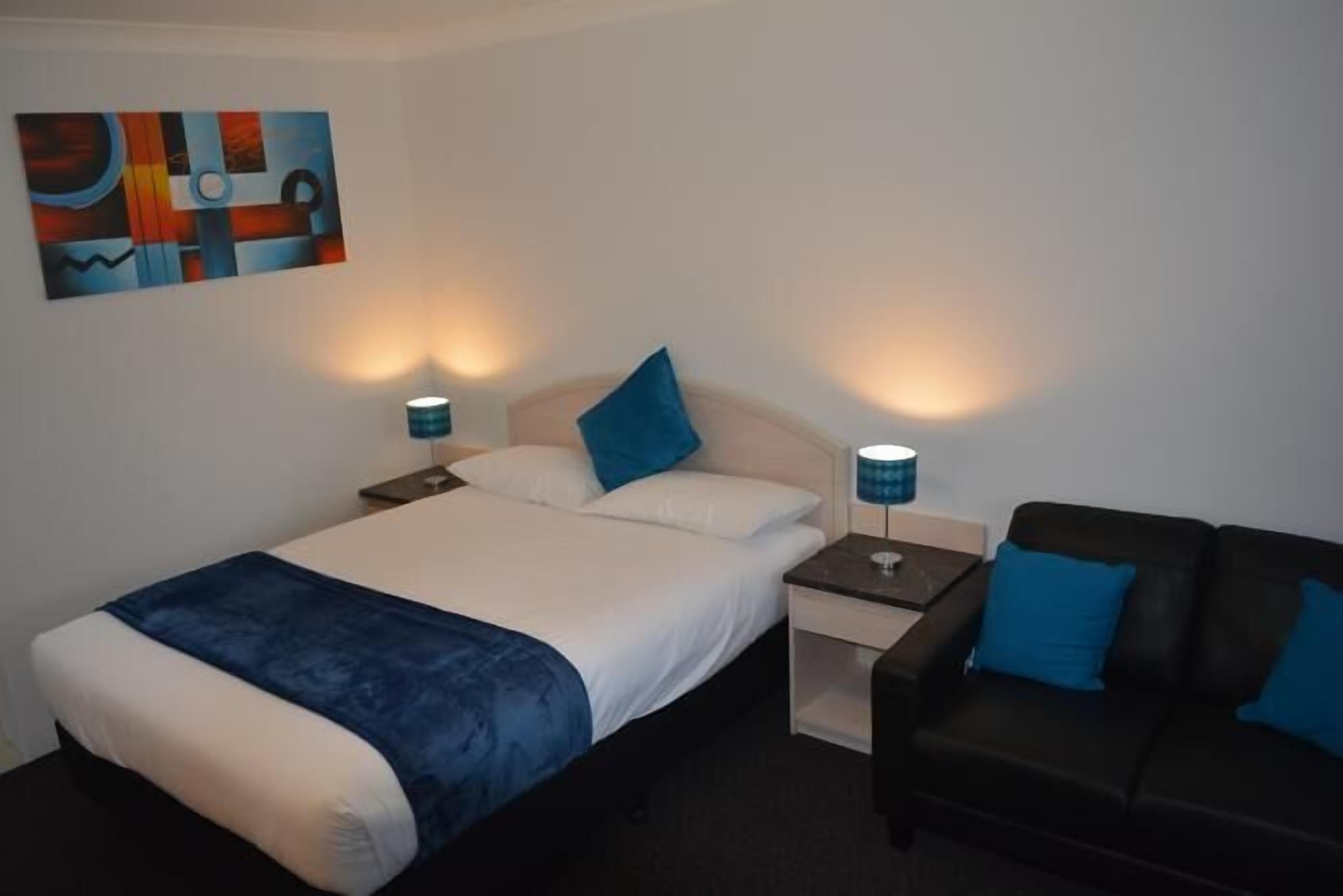 Una camera d'albergo con un letto, un comodino, una lampada, un divano e un quadro appeso al muro.
