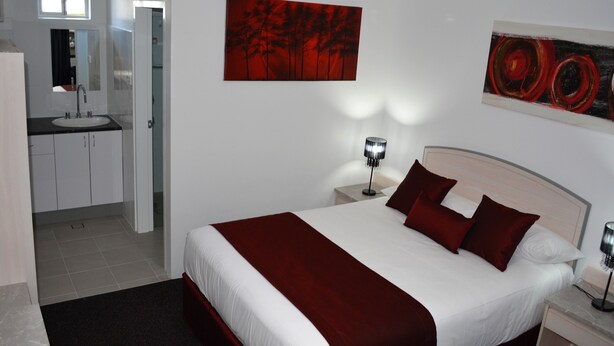 A hotel room with a large bed, two bedside tables, a nightstand, a window, a bathroom with a sink and mirror, and two paintings on the wall. - Alabaster Motor Inn Taree (Taree)
