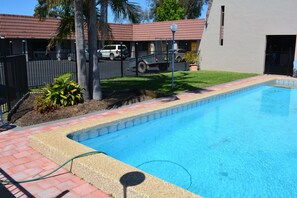 A swimming pool with a tiled edge, surrounded by a brick patio and a metal fence.