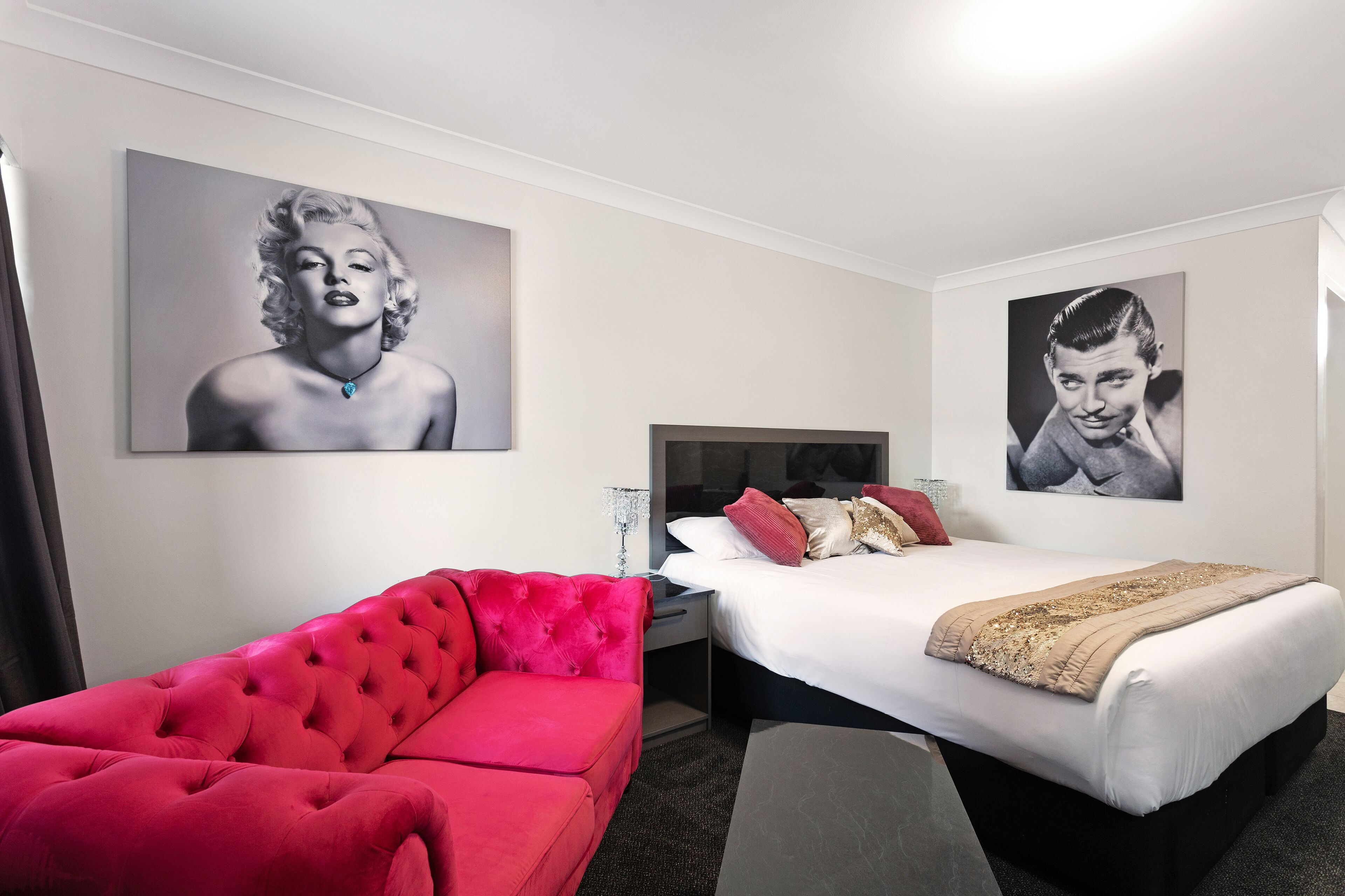 Ein Hotelzimmer mit einem roten Sofa, einem Bett mit weißer Bettwäsche und zwei großen, gerahmten Bildern an den Wänden.