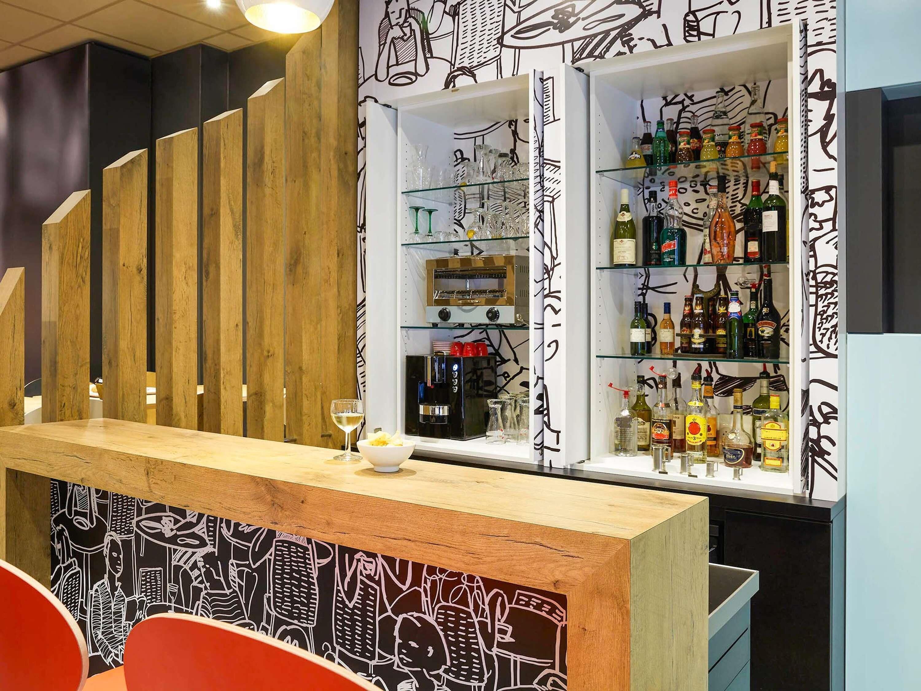 Zona de bar con mostrador de madera, estanterías con botellas y una pared decorada con obra de arte blanco y negro.