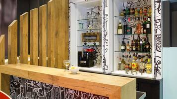Zona de bar con mostrador de madera, estanterías con botellas y una pared decorada con obra de arte blanco y negro.