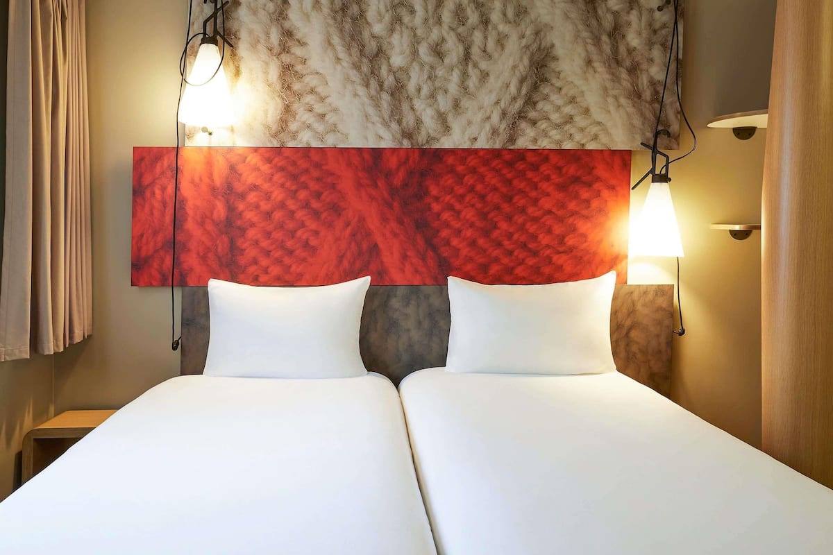 A double bed with white linens, a red textured headboard, and two bedside lamps.