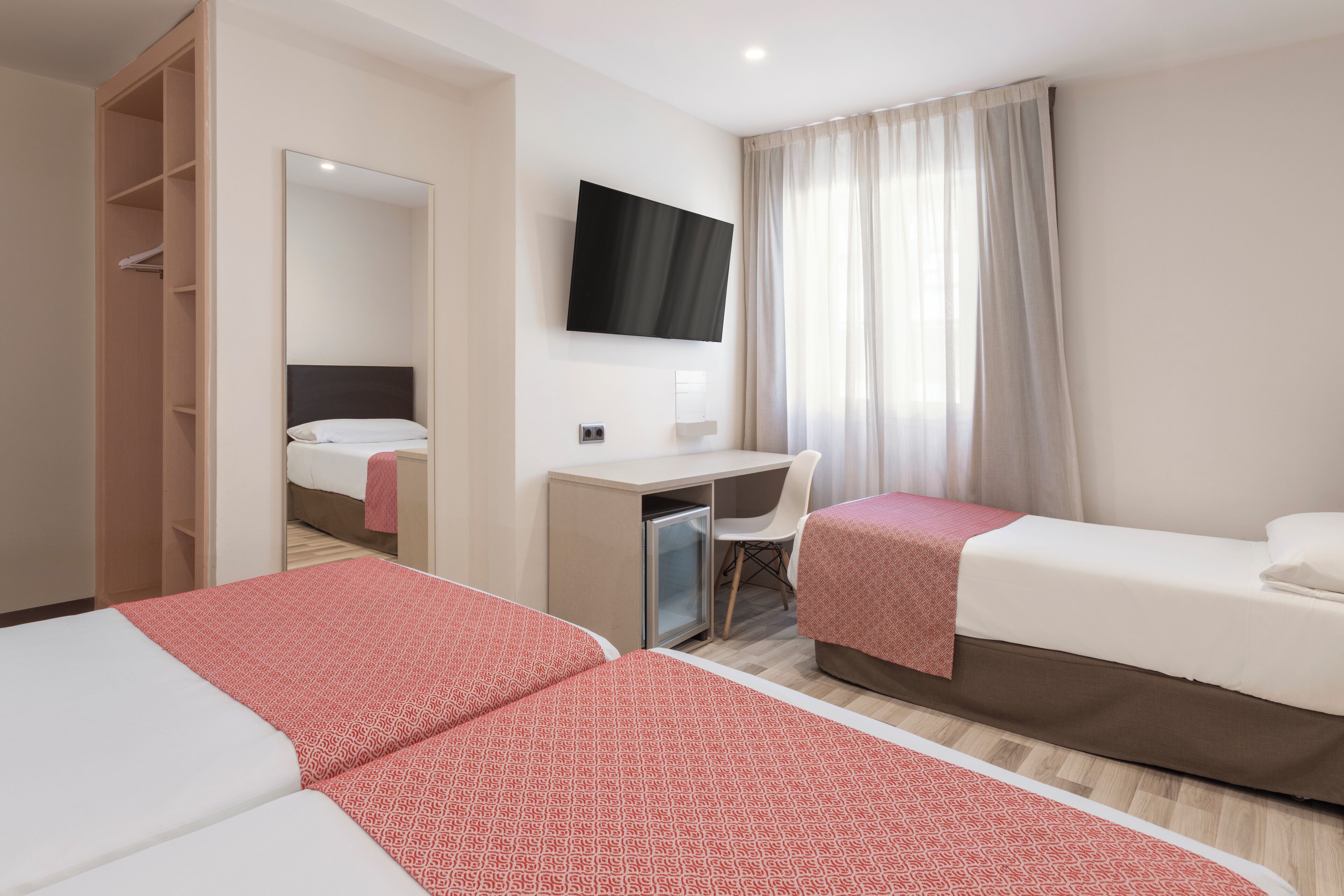 A hotel room with two beds, a desk, a chair, a TV, and a wardrobe.