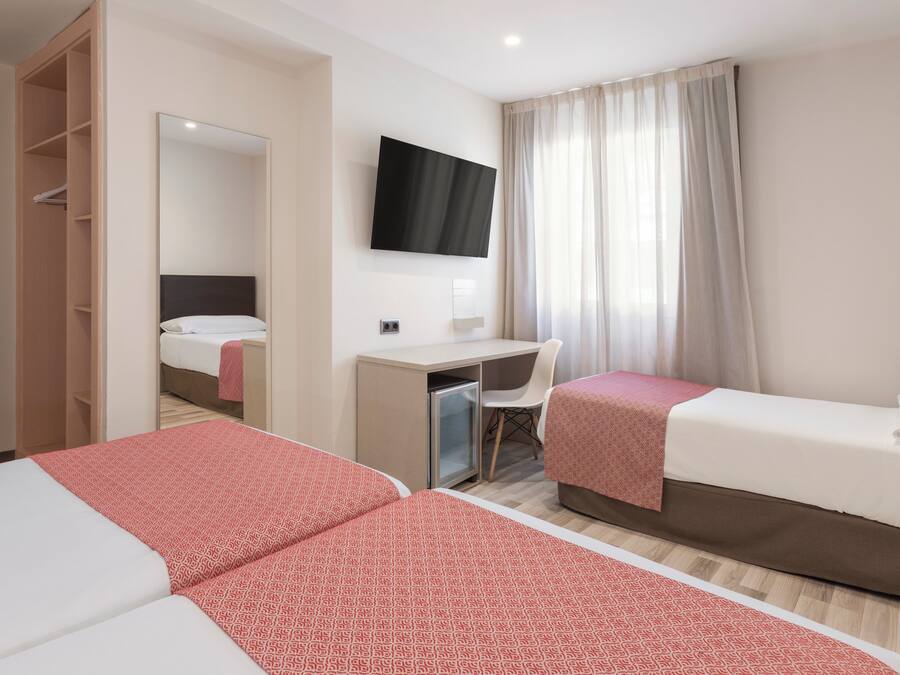A hotel room with two beds, a desk, a chair, a TV, and a wardrobe.
