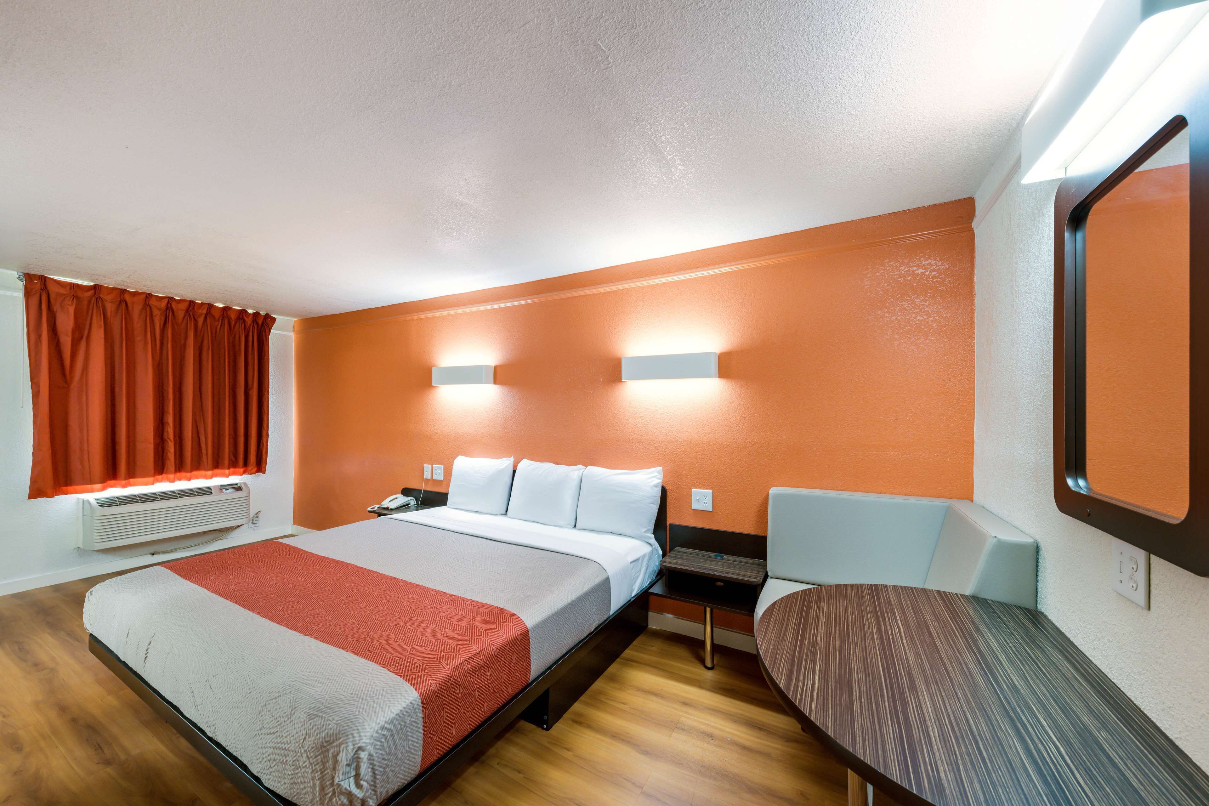 A hotel room with a bed, bedside table, chair, and a large mirror.