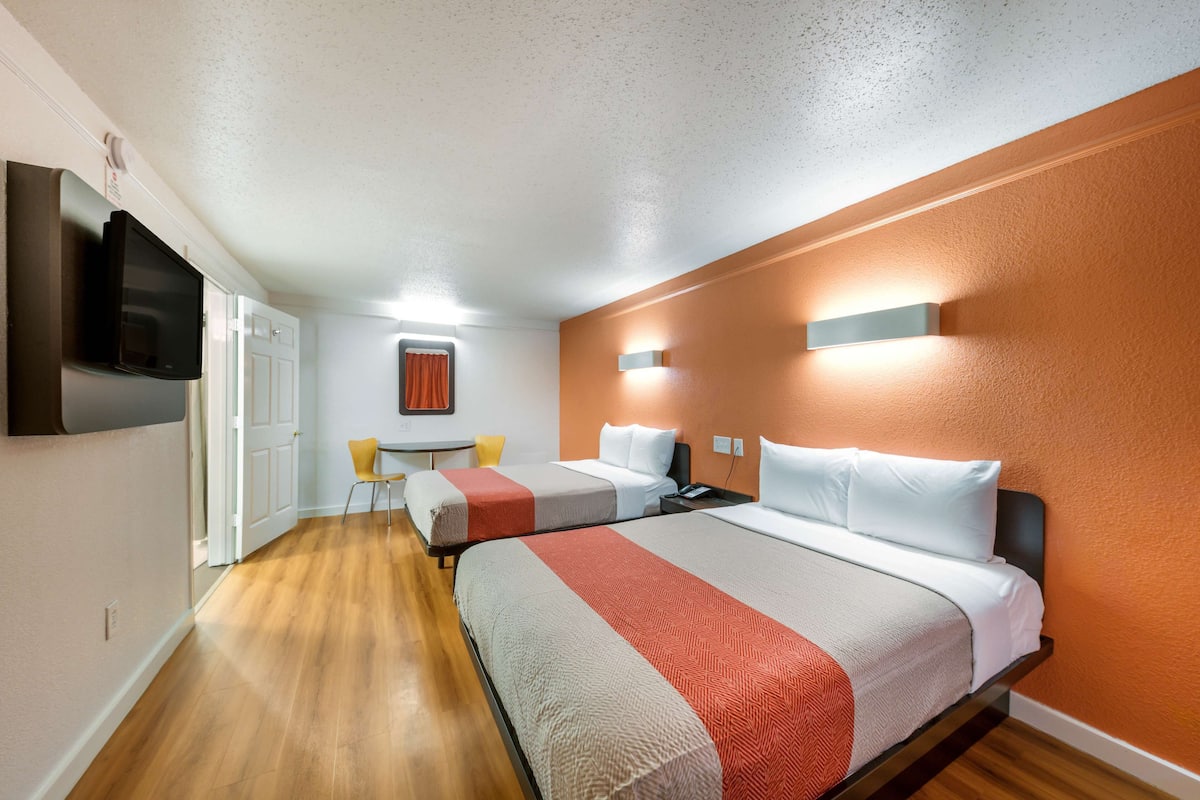 A hotel room with two beds, a TV, a small table, and a chair.