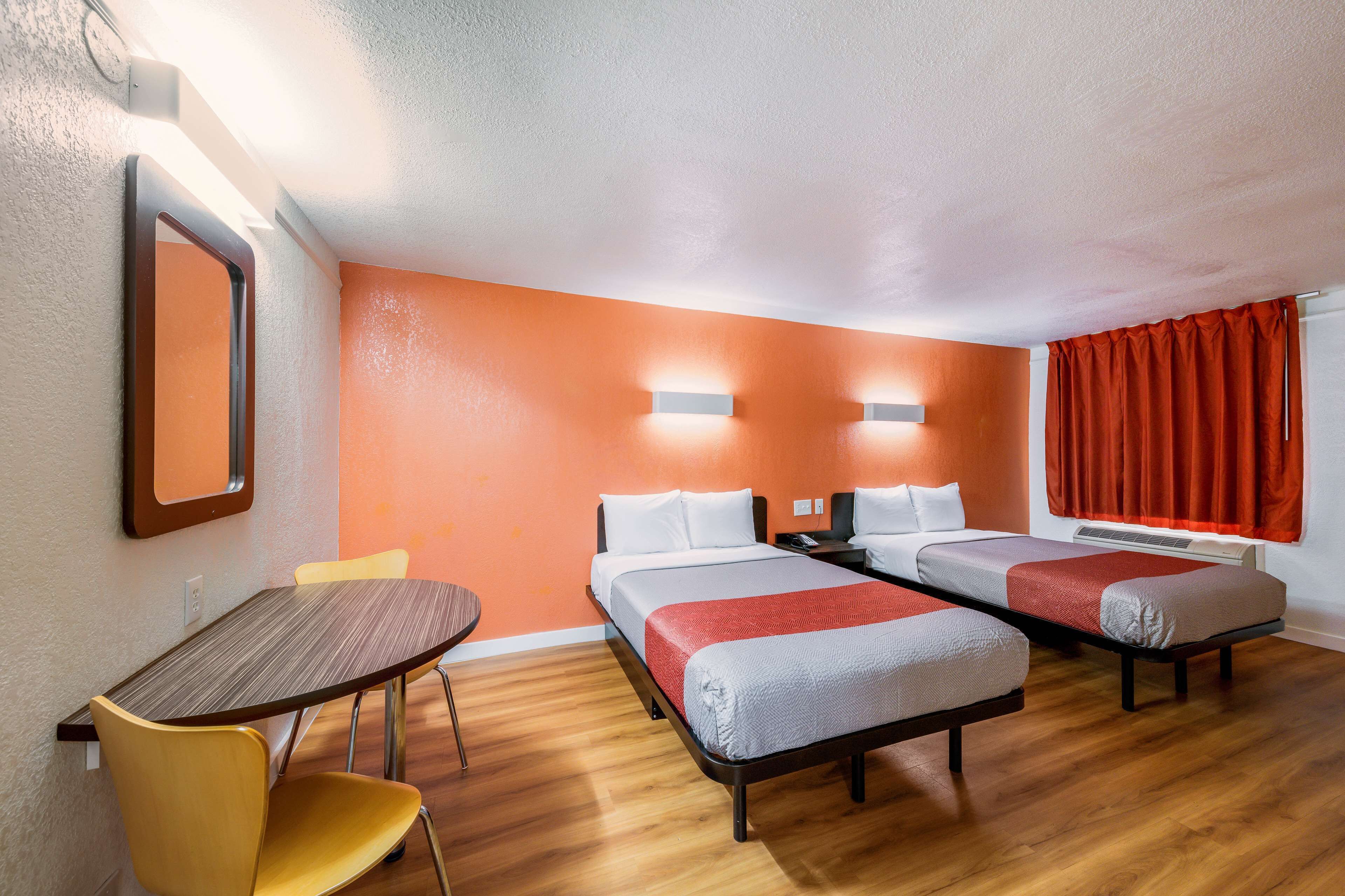 A hotel room with two single beds, a wooden table, a yellow chair, and a mirror on the wall.