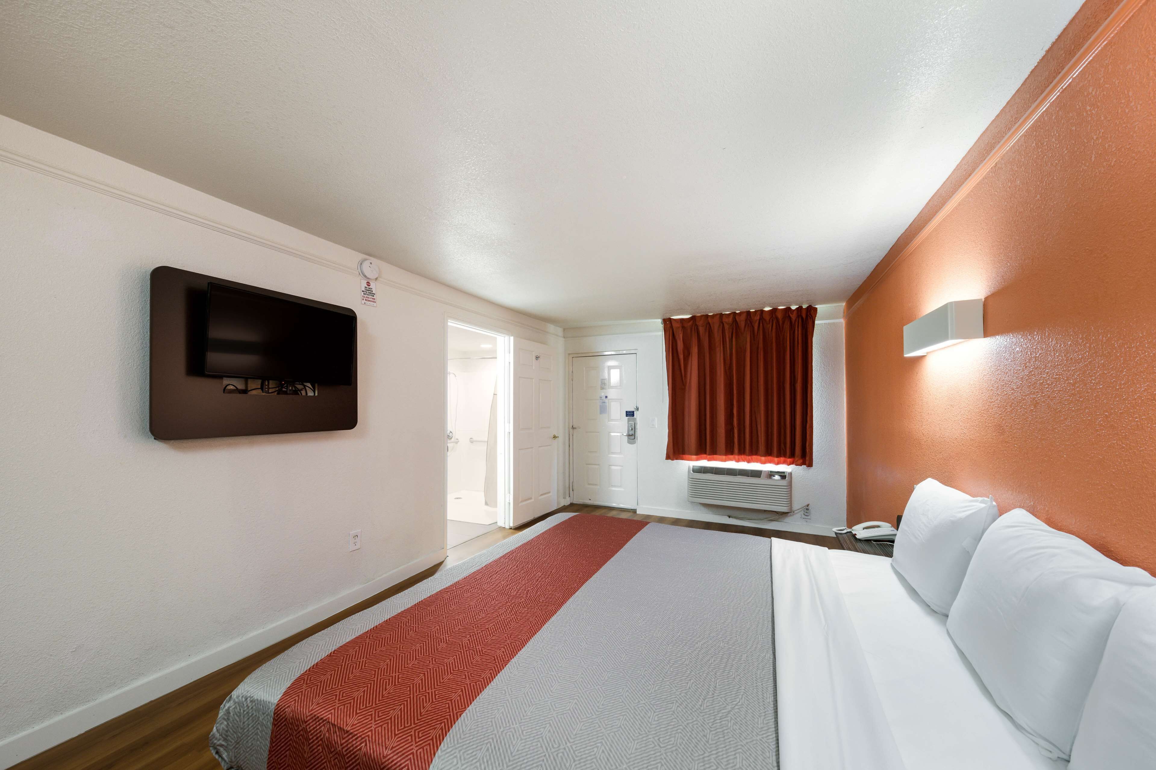 Une chambre d’hôtel dotée d’un grand lit, d’un téléviseur à écran plat fixé au mur, d’une fenêtre avec des rideaux et d’un thermostat mural.