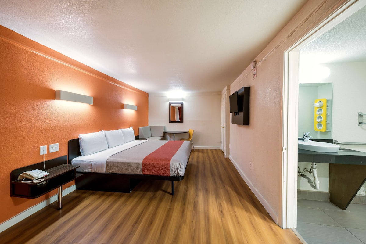 A hotel room with a bed, bedside table, and a bathroom with a sink and mirror.