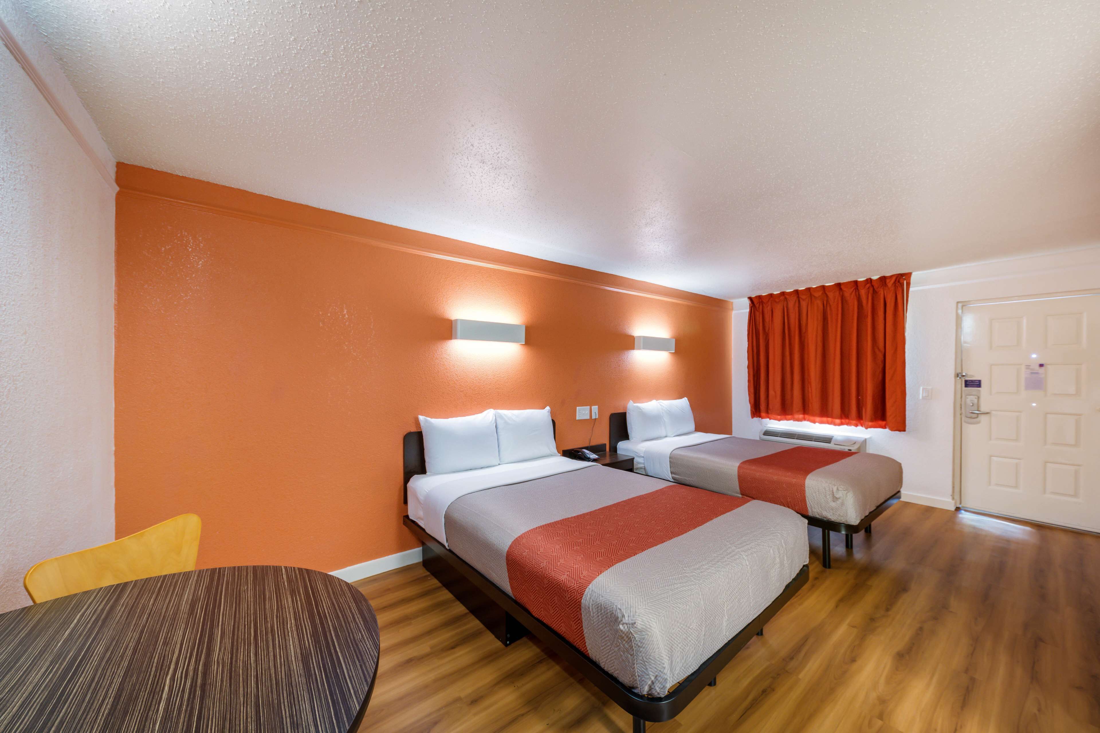 A hotel room with two beds, a wooden floor, and a single chair.
