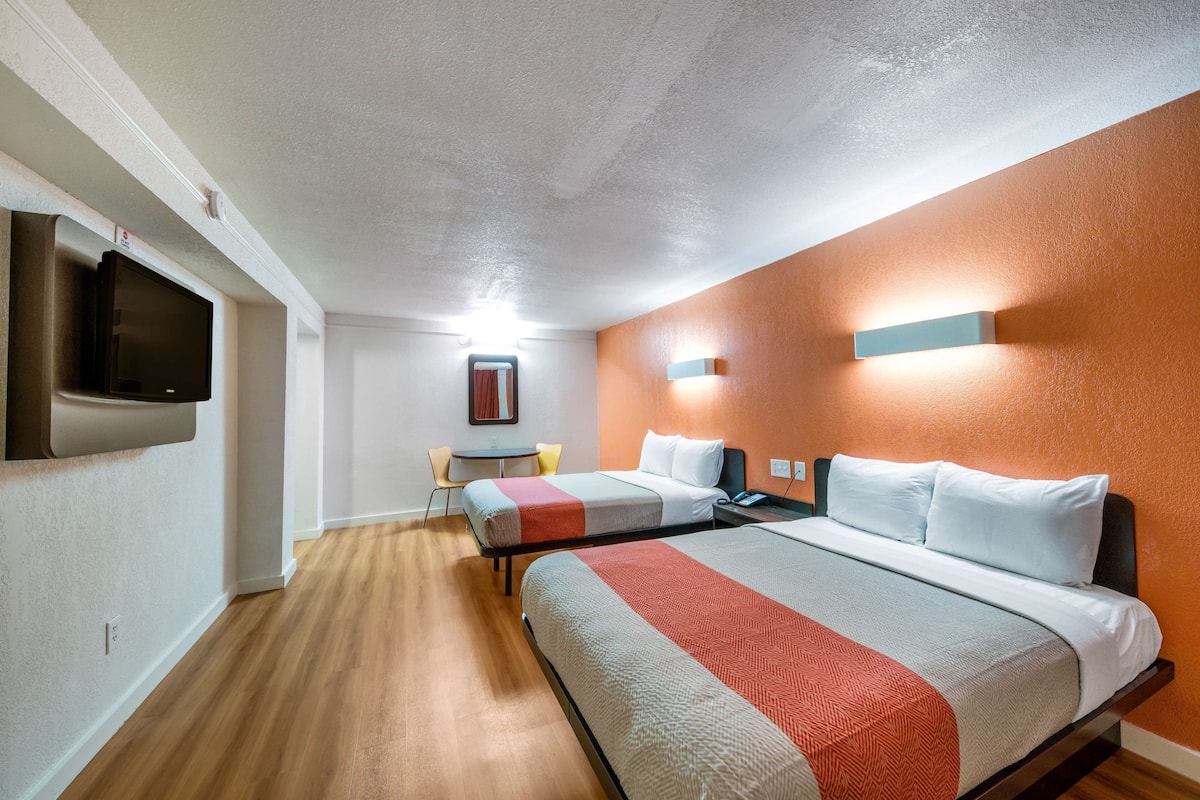 A hotel room with two beds, a TV, a desk, and a chair.
