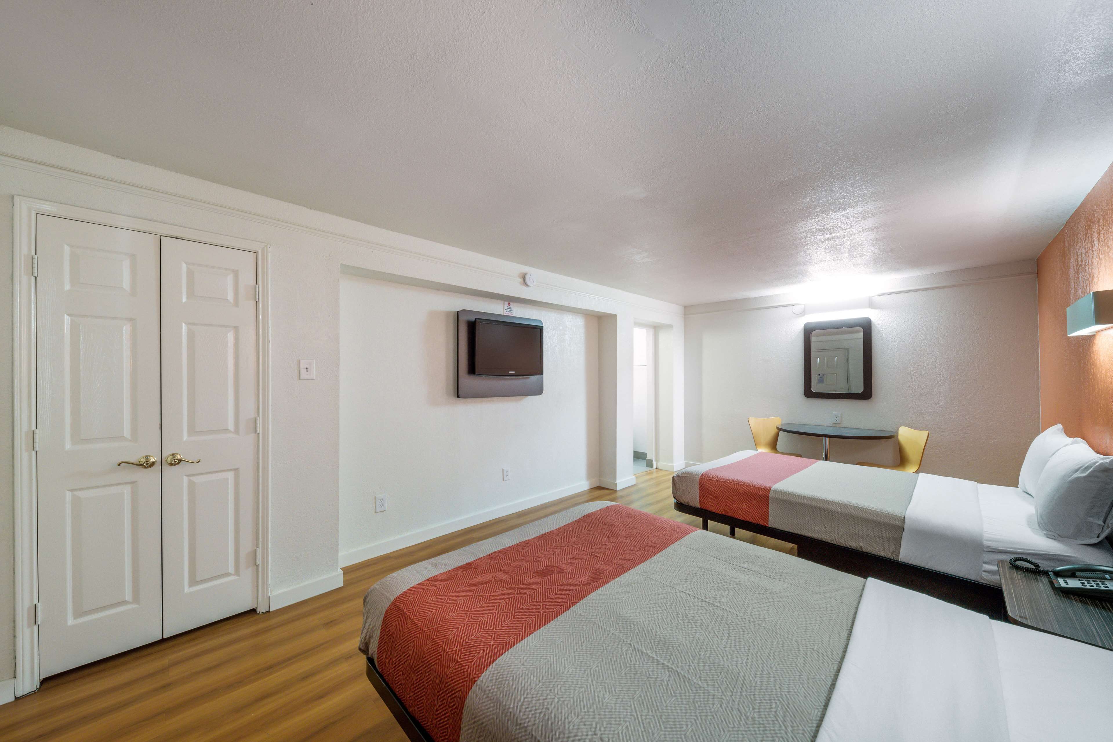 A hotel room with two beds, a TV, a small table, and a desk with a chair.