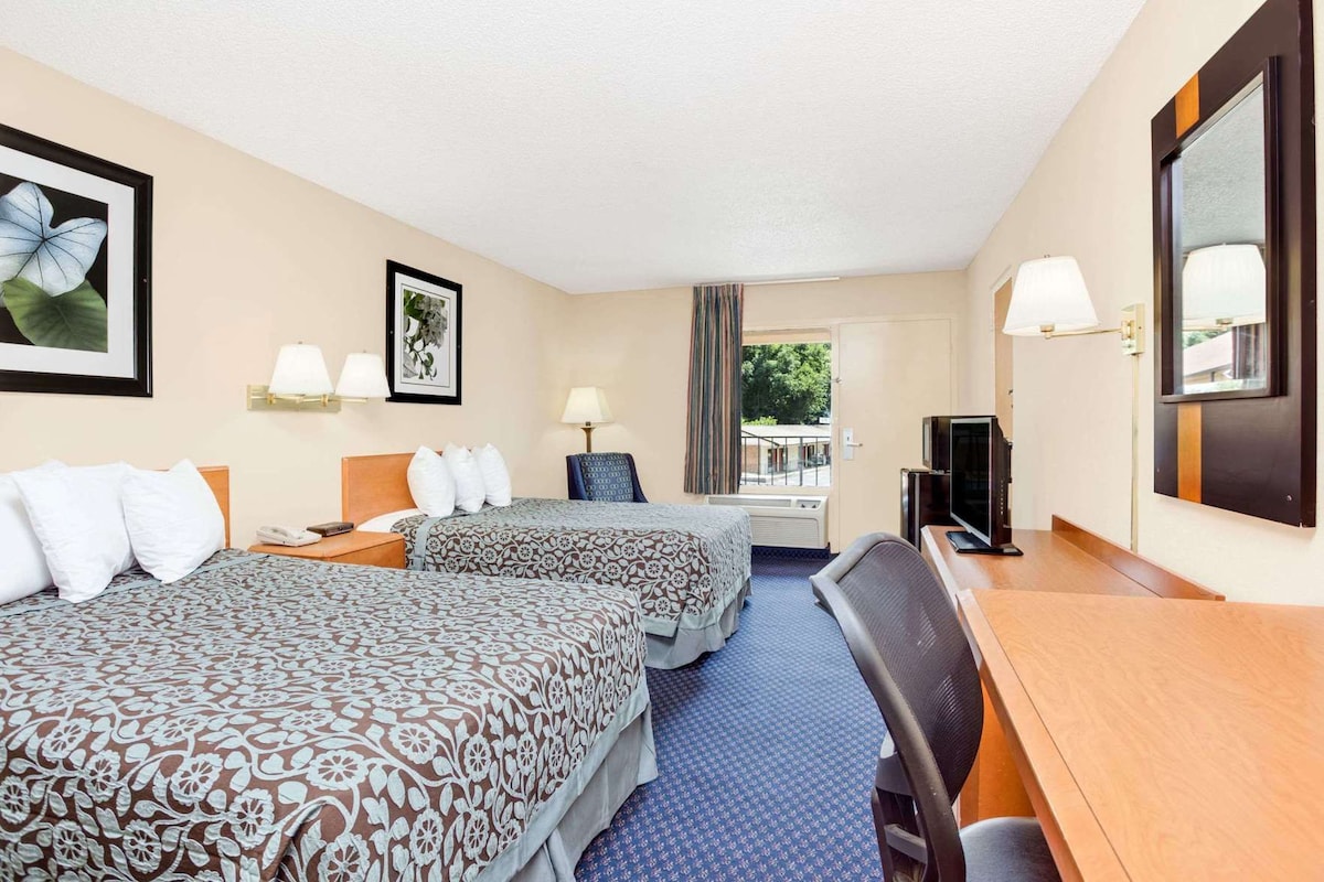 A hotel room with two beds, a desk with a TV, a chair, and a window with a view.
