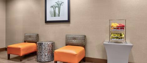 A room with two orange cushioned seating areas, a framed artwork on the wall, and a fruit display on a pedestal.