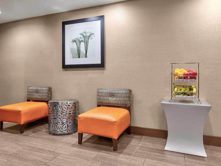 A room with two orange cushioned seating areas, a framed artwork on the wall, and a fruit display on a pedestal.