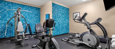A gym with exercise equipment, including a stationary bike, elliptical, and weight machine.