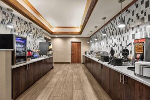 Un espace pour le petit-déjeuner dans un hôtel, avec un long comptoir, différents buffets et une porte en bois.