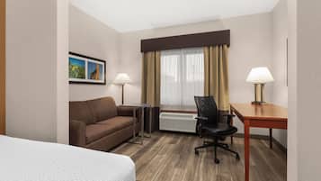 Habitación de hotel con cama, sofá, escritorio, silla, radiador y ventana con cortinas.