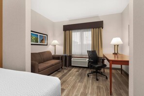 Een hotelkamer met een bed, een bank, een bureau, een stoel, een radiator en een raam met gordijnen.