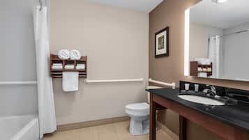 A bathroom with a shower, toilet, and sink. There are towels on a shelf and a framed picture on the wall.