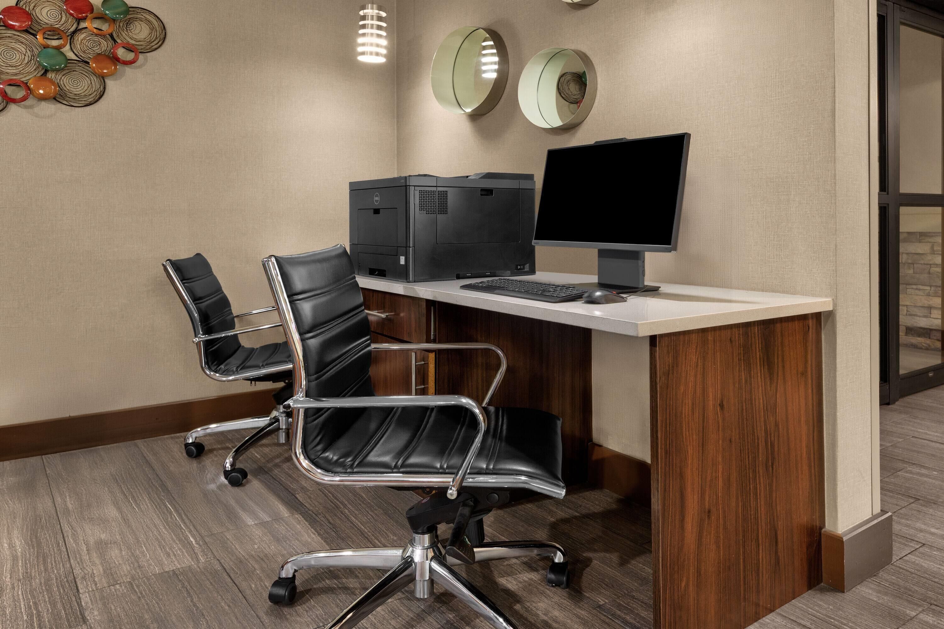A conference room with a wooden desk, two black office chairs, a desktop computer, and a printer.