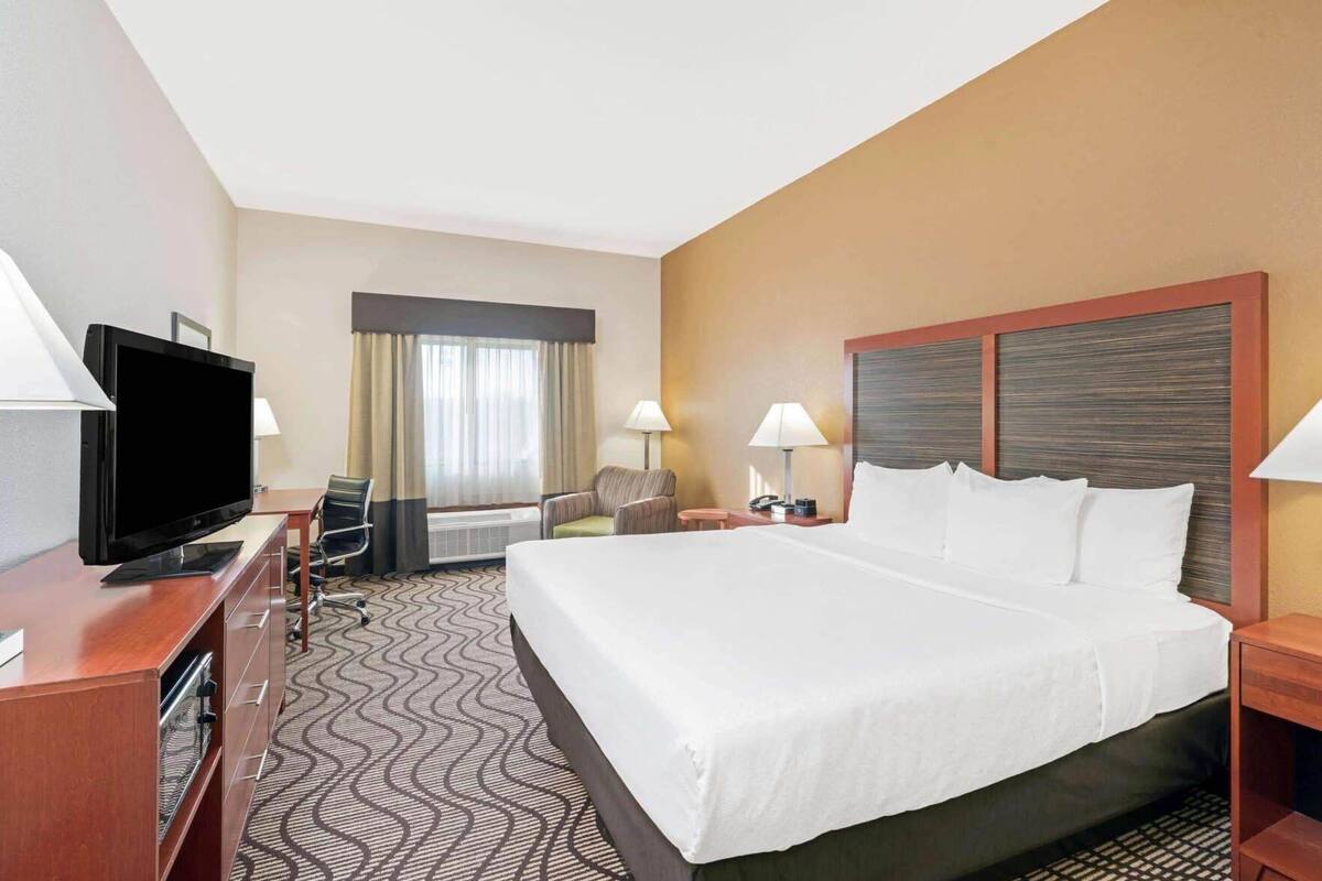 Een hotelkamer met een groot bed, een flatscreen televisie, een bureau met stoel, een lamp en een raam met gordijnen.