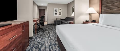Habitación de hotel con cama, televisor, escritorio, silla y lámpara.