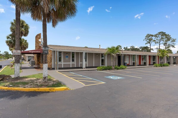 A motel with a registration desk, a parking lot with handicapped parking, and a building with a beige facade and red doors. - Super 8 by Wyndham Kissimmee/Orlando (Kissimmee)