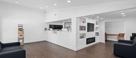 A spacious living area with a wooden floor, a reception desk, a TV, and a bookshelf.