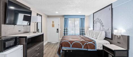 A modern hotel room with a bed, a desk, a microwave, and a TV.